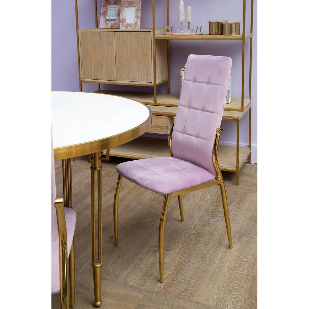 Pink velvet dining chair with gold metal frame beside round white and gold dining table