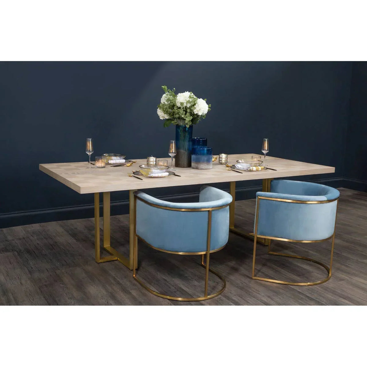 Modern dining table with light wood top, gold frame and two blue velvet dining chairs
