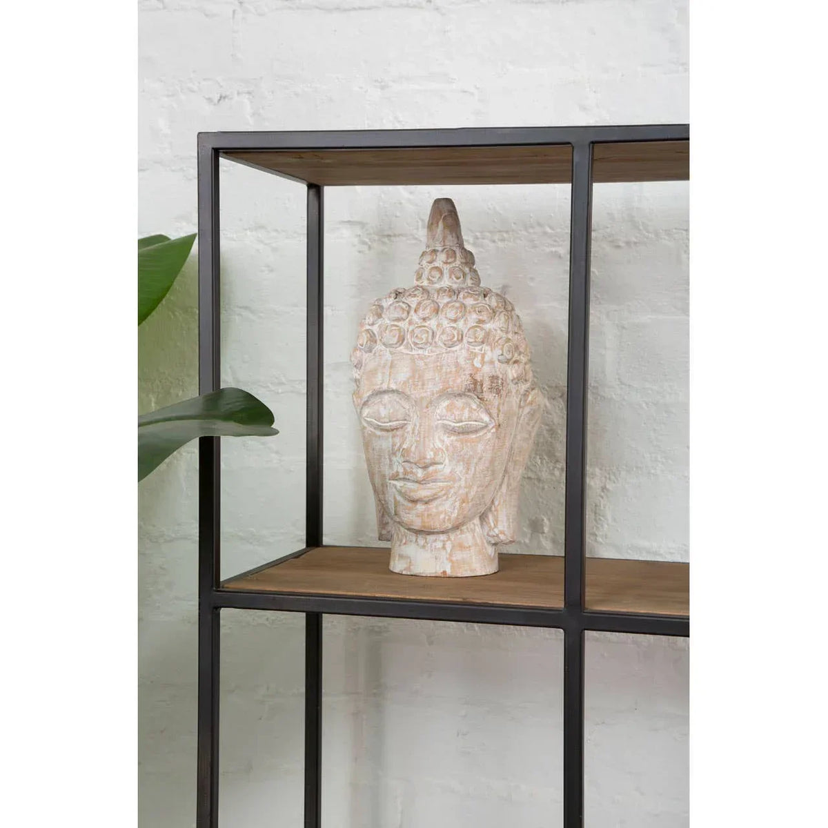 Carved Buddha head sculpture on metal and wood shelf against white brick wall