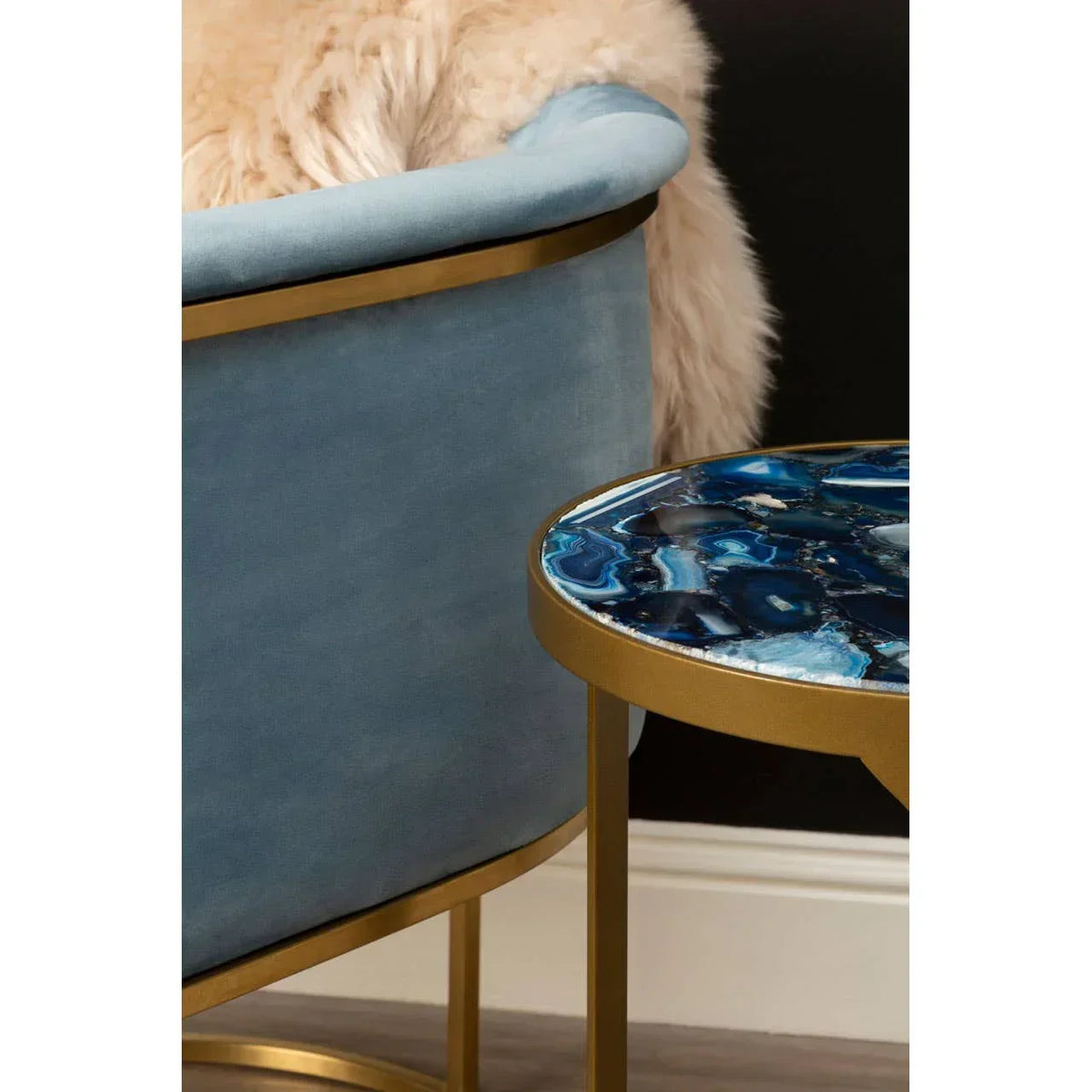 Blue velvet accent chair with gold trim beside round blue agate side table