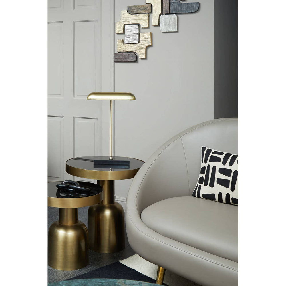 Brown leather effect 3 seater sofa positioned in a modern living space, accompanied by stylish gold accent tables and a contemporary floor lamp. The background features a light-colored wall with decorative wall art, creating a cozy and elegant atmosphere