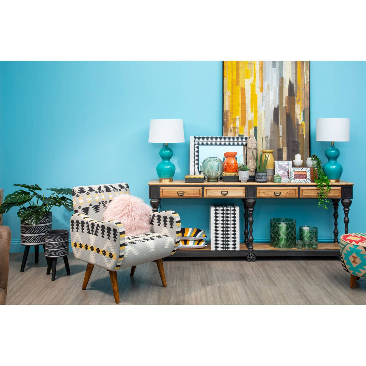 A stylish black and white resin table and stool set placed in a vibrant room with a turquoise wall. The table features a sleek design, complementing the modern decor, while the stool has a matching aesthetic. In the background, there is a console table adorned with decorative items, a colorful painting, and two lamps, creating a cozy and inviting atmosphere