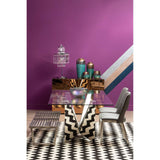 A stylish console table with a tinted mirror surface, set against a vibrant purple wall. The table is adorned with decorative vases in various colors, and a patterned rug featuring black and white stripes underneath. The overall aesthetic is modern and chic, with a mix of textures and colors