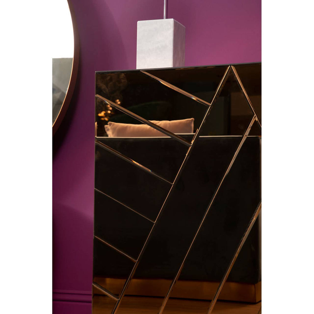 A stylish console table featuring a tinted mirror surface with geometric patterns and a sleek black base. The table is positioned against a vibrant purple wall, complemented by a modern pendant light hanging above
