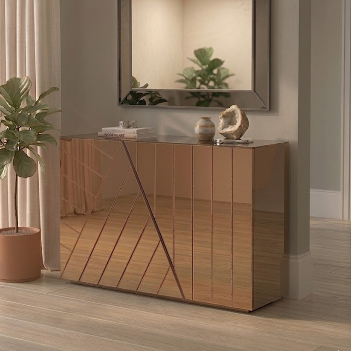 A modern console table with a tinted mirror finish, featuring a geometric design on the front. The table is positioned against a light-colored wall, with a decorative mirror above it. A potted plant is placed beside the table on the floor, enhancing the contemporary aesthetic of the room. The flooring is light wood, adding warmth to the space
