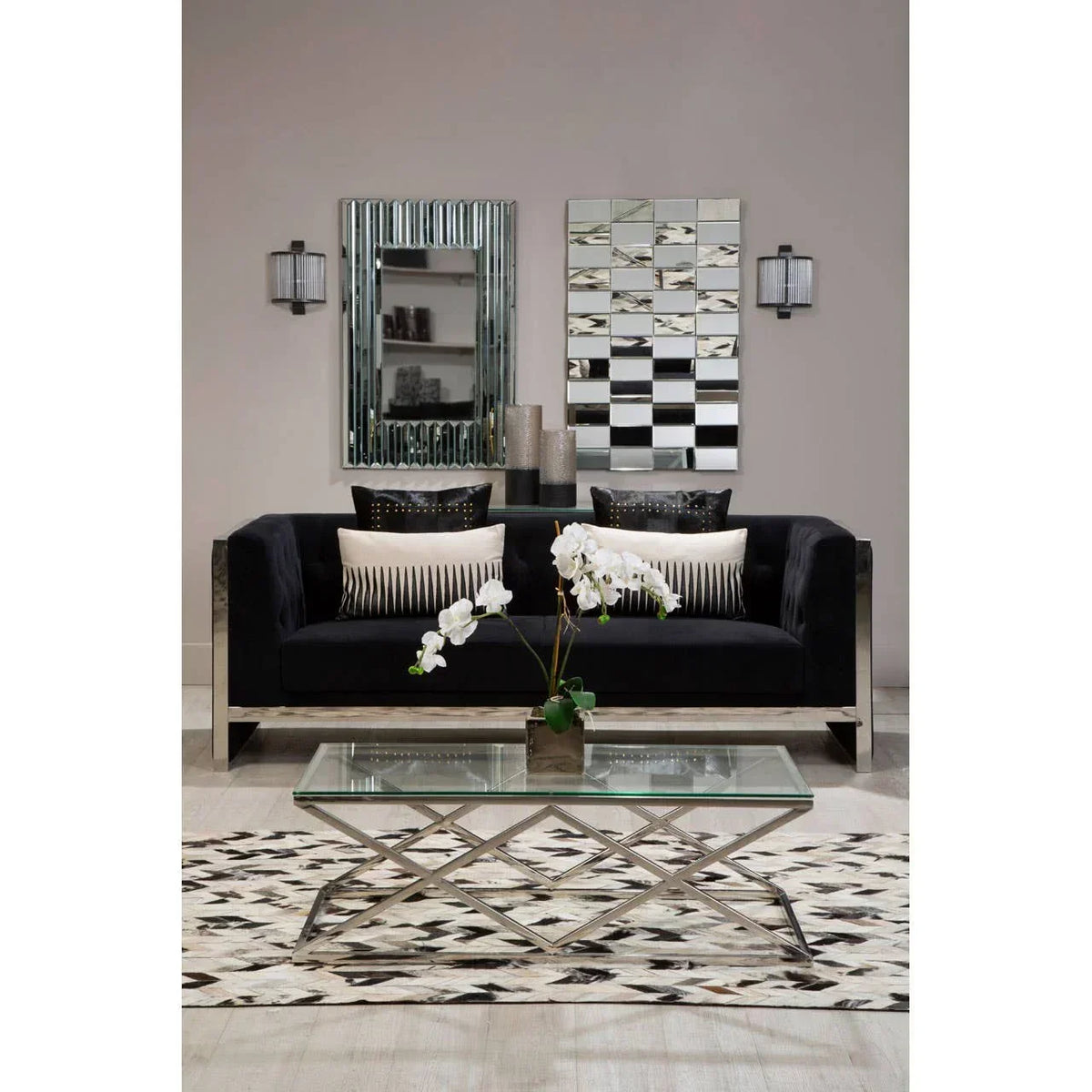 Modern black velvet sofa with chrome frame and cushions, glass coffee table, geometric rug