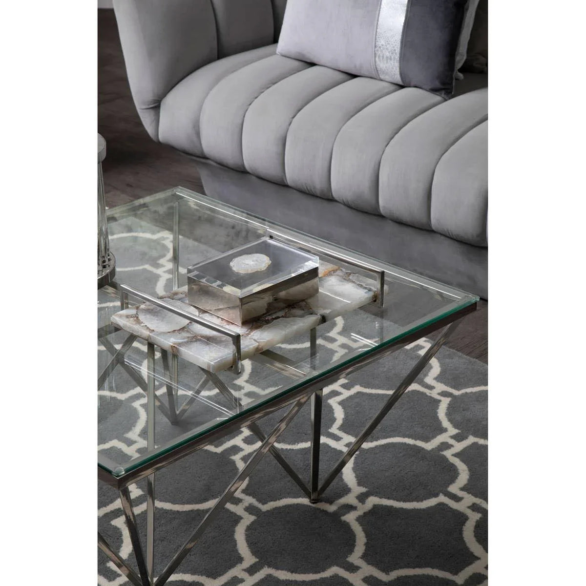 Glass coffee table with chrome legs and marble tray beside a grey velvet sofa on patterned rug