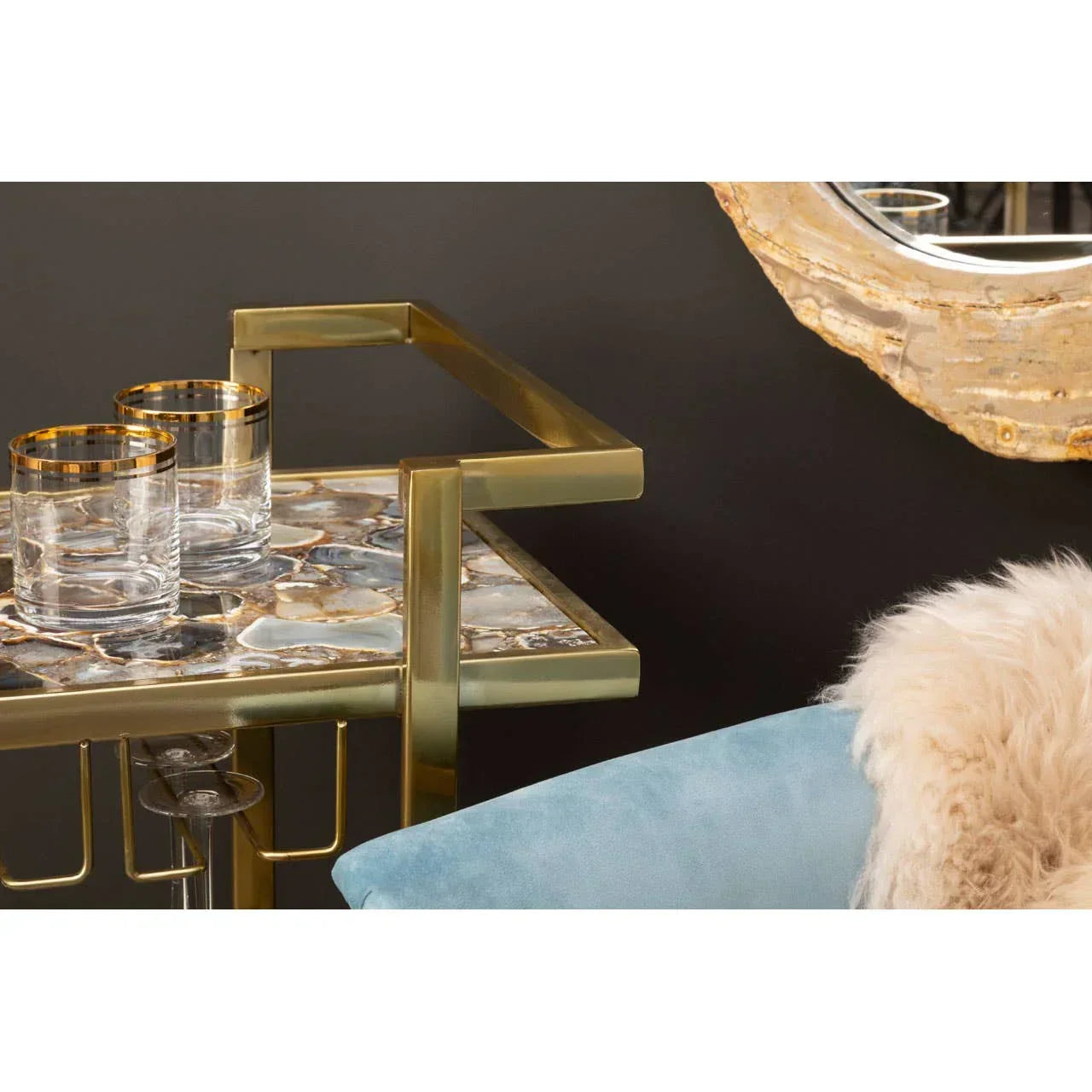 Gold metal and stone drinks trolley with two glasses beside blue velvet chair