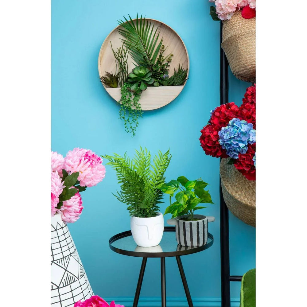 Indoor plant display with potted artificial foliage and wall-mounted planter on glass table