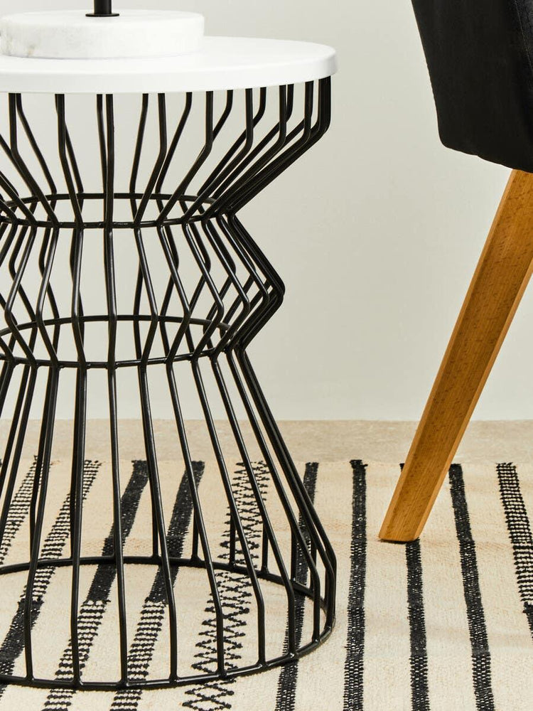 Modern round side table with black wire metal base and white top on striped rug