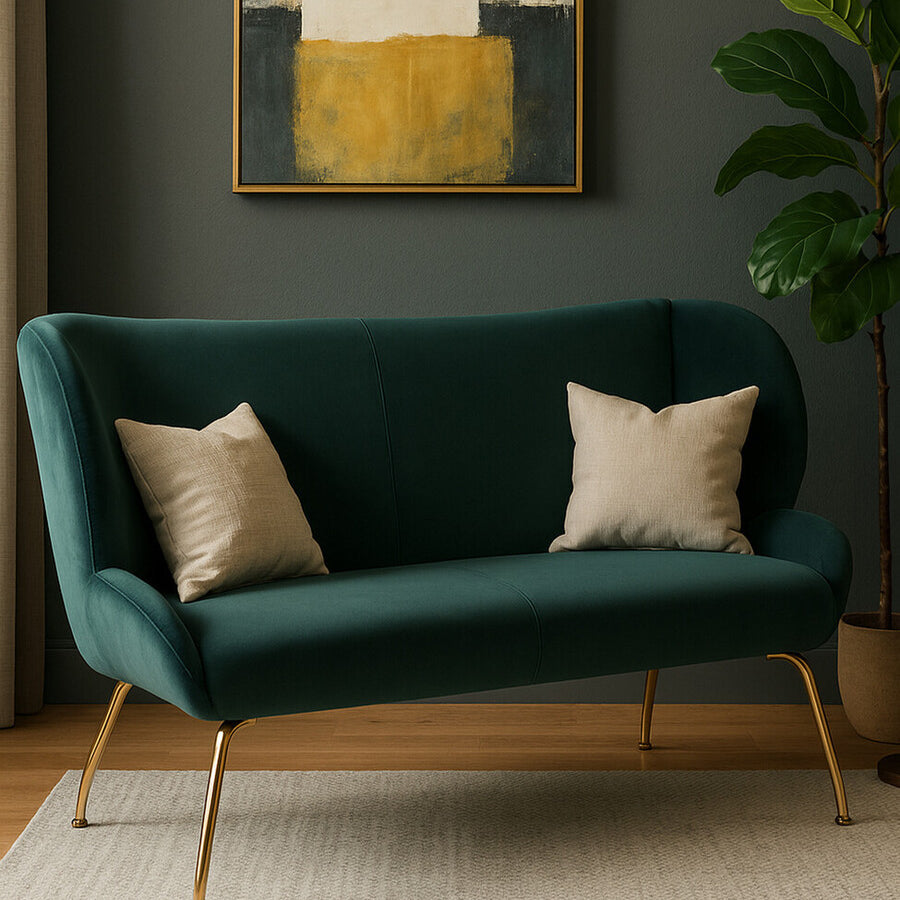 A stylish green two-seat sofa with a curved backrest, featuring two light-colored decorative pillows. The sofa is set against a dark wall and is accompanied by a large abstract painting above it and a potted plant nearby. A light-colored rug is placed underneath the sofa, enhancing the cozy atmosphere of the room