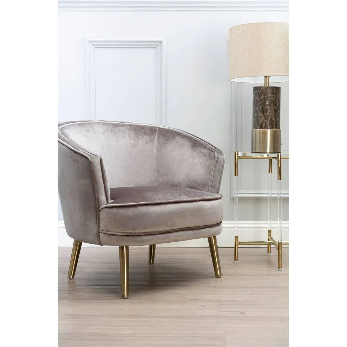 Velvet accent chair with gold legs beside marble table lamp on acrylic side table