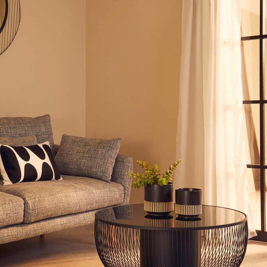 Modern black wire coffee table with glass top beside grey sofa in living room