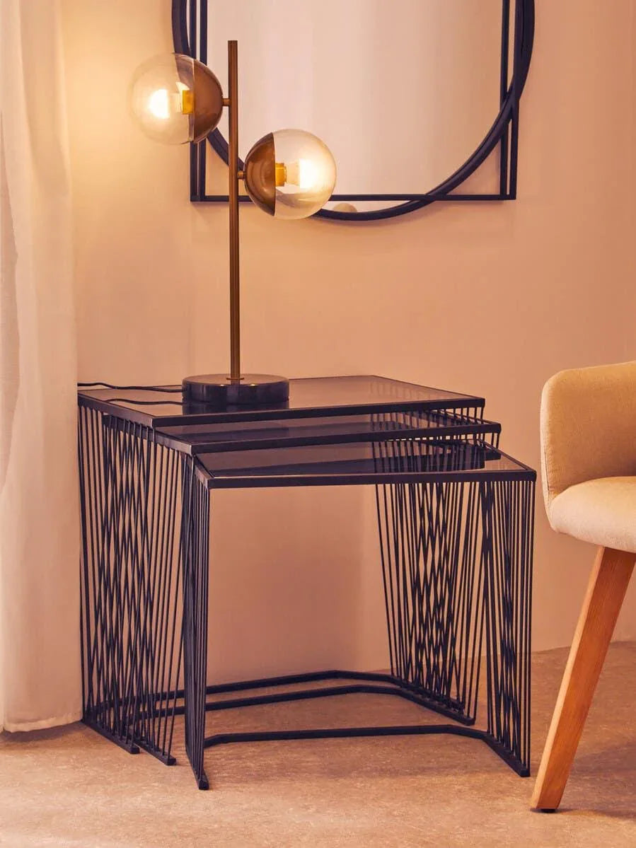 Black metal nesting tables with glass tops beside beige chair and modern table lamp