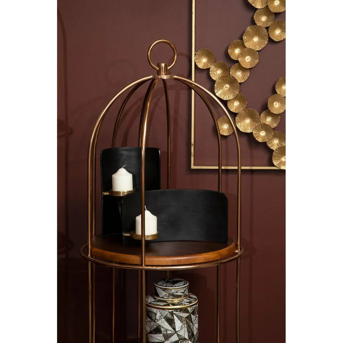 Gold metal side table with decorative candles and geometric storage jar against dark red wall