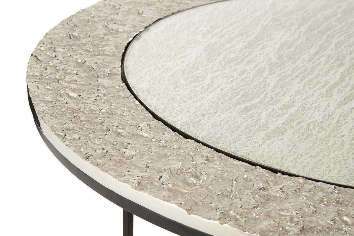 Round coffee table with textured metallic edge and frosted glass top, close-up view