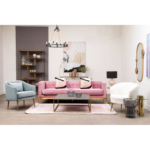 Three-seat pink sofa with plush cushions, positioned in a stylish living room setting alongside a light blue armchair and a white accent chair. A coffee table with a decorative centerpiece sits in front of the sofa, and a patterned area rug adds warmth to the space. Wall art and a bookshelf are visible in the background, creating a cozy atmosphere
