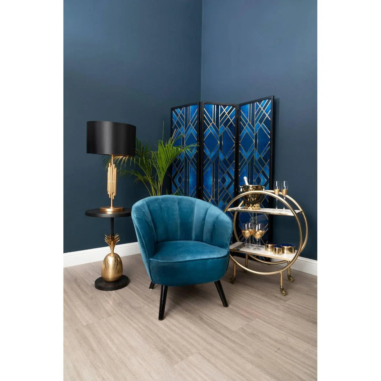 Blue velvet accent chair with black legs beside gold drinks trolley and art deco room divider