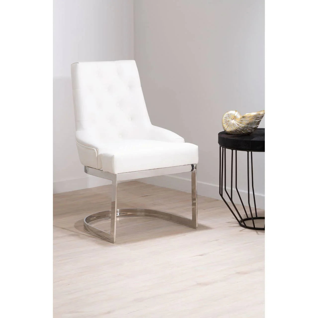 White accent chair with chrome base and tufted back beside black side table on light flooring