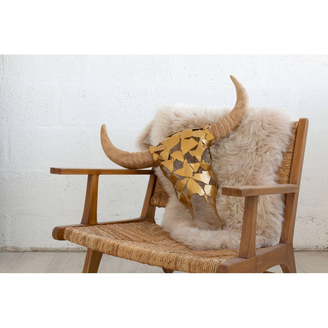 Wooden armchair with woven seat, sheepskin throw, and gold decorative bull skull