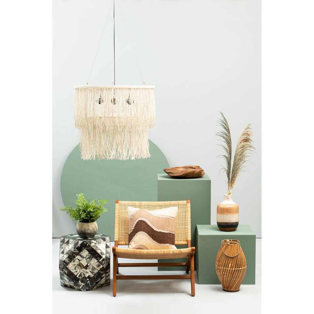 A stylish lounge chair featuring a wooden frame and natural rattan seat, positioned in a decorative setting with green and neutral tones. The background includes a large circular green accent, a woven wall hanging, and various decorative items such as potted plants and sculptural objects on stacked boxes