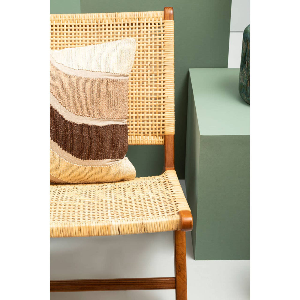 A wooden lounge chair featuring a natural rattan seat and backrest, accompanied by a decorative pillow with a geometric pattern in soft colors. The chair is positioned next to a green side table, set against a muted wall backdrop