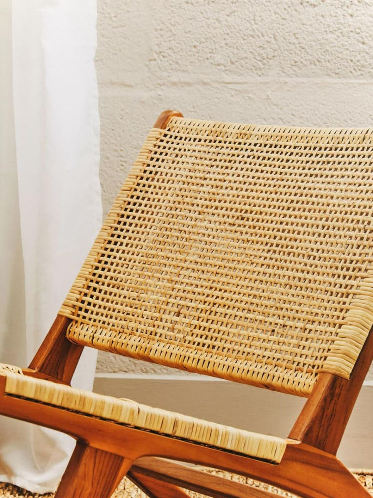 Natural rattan seat of a lounge chair with a wooden frame, showcasing a woven texture and warm tones, set against a light-colored wall