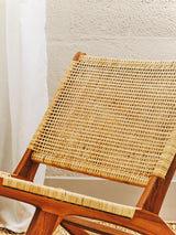 Natural rattan seat of a lounge chair with a wooden frame, showcasing a woven texture and warm tones, set against a light-colored wall