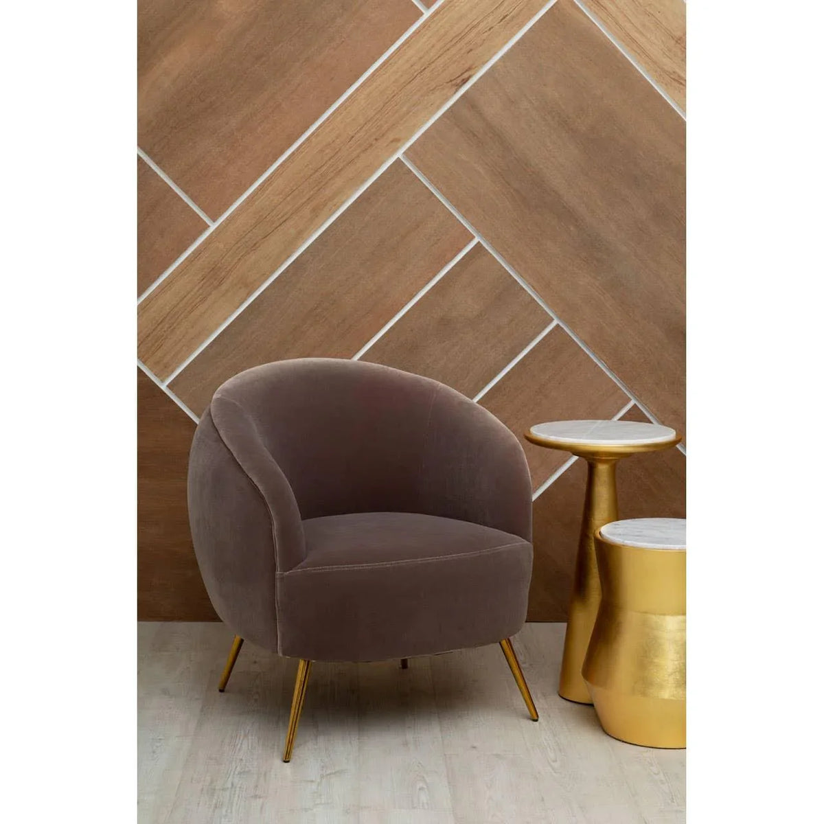 Grey velvet accent chair with gold legs beside two gold and marble side tables