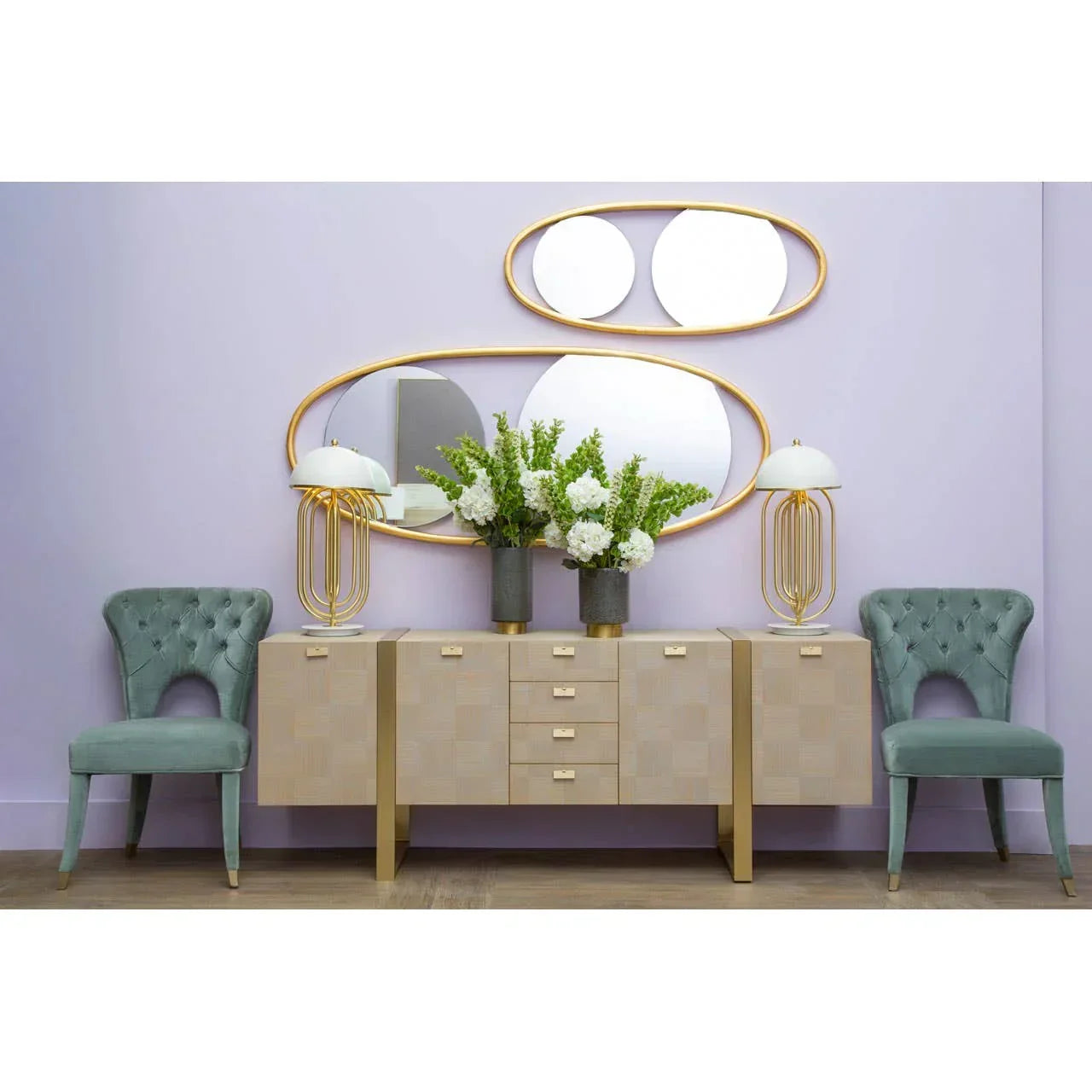 Modern sideboard with gold accents, oval mirrors, two green chairs, and floral arrangements