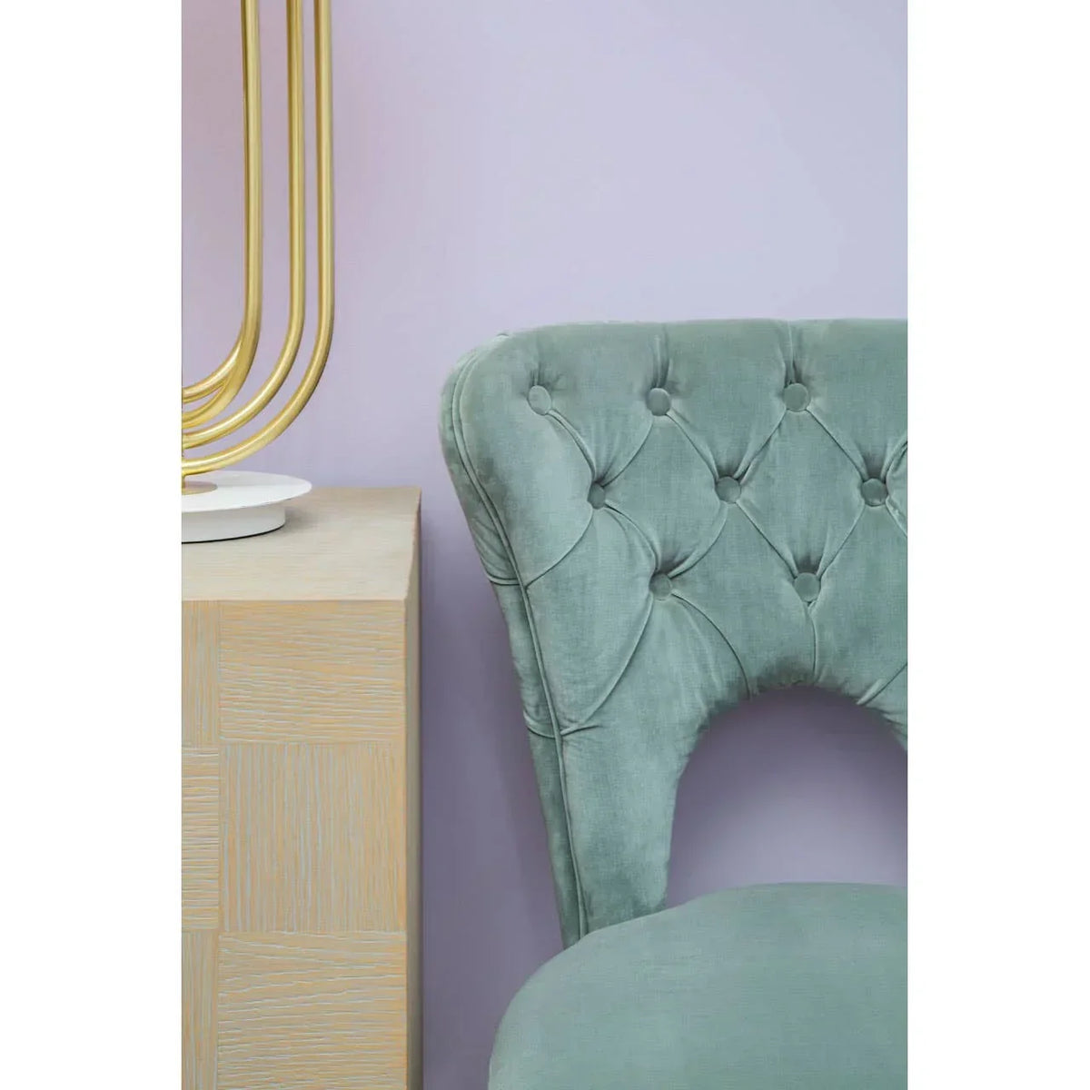 Green velvet dining chair with button tufting next to light wood side table and gold lamp