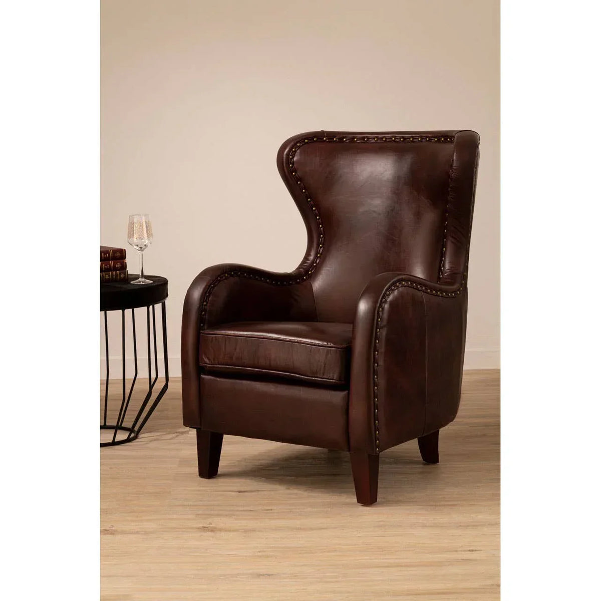 Brown leather accent armchair with nailhead trim and wooden legs beside round black side table
