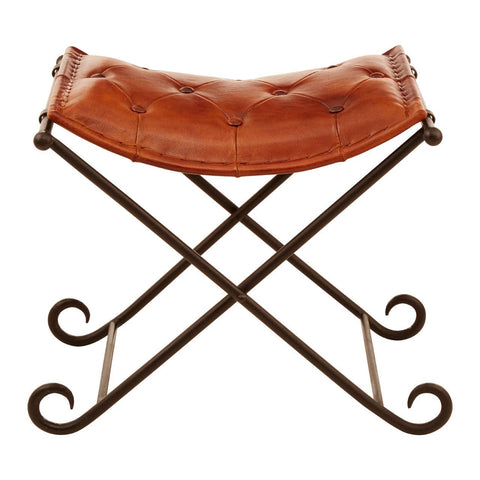 Buffalo tan leather folding stool with a curved seat and an iron frame featuring an elegant cross design and scroll accents on the legs