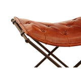 Buffalo tan leather folding stool featuring a tufted seat and a sturdy iron frame with a cross-legged design, showcasing a warm, rustic aesthetic
