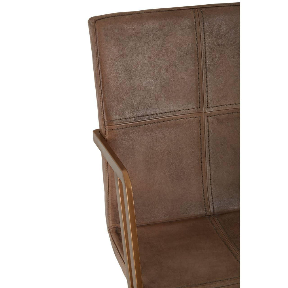 Brown leather armchair closeup with gold metal armrest and square stitched backrest