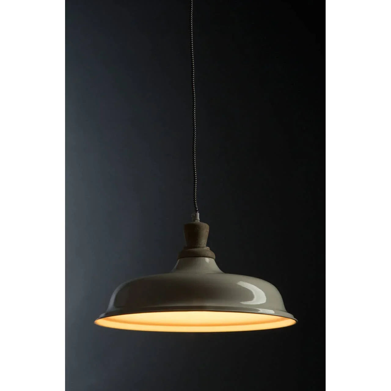 Grey pendant light with wooden top and warm glow suspended against a dark background