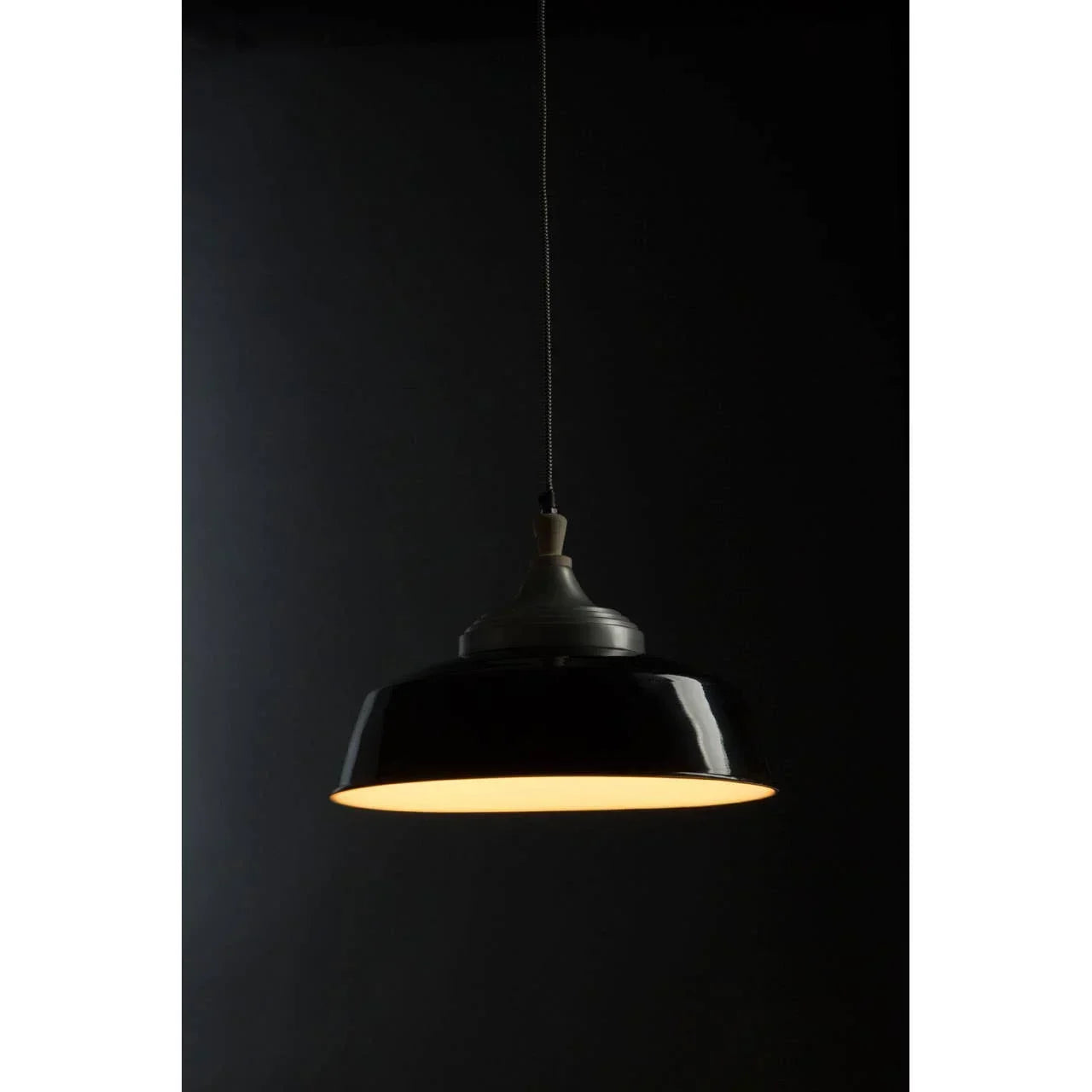 Black metal pendant ceiling light with warm glow against dark background