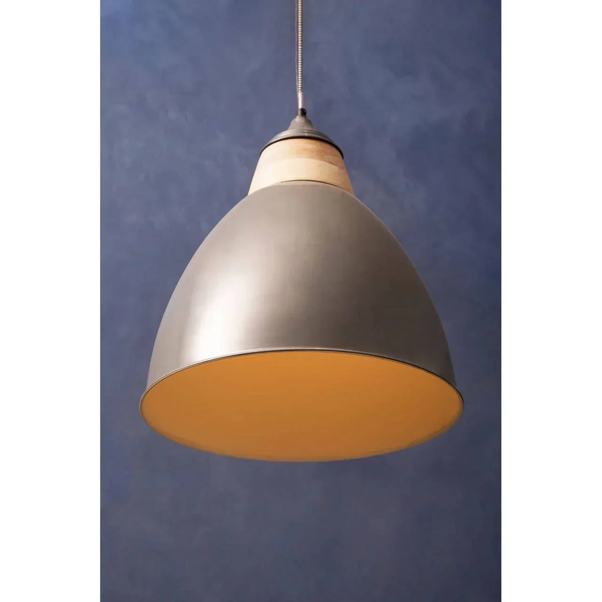 Grey metal pendant light with wooden accent hanging against blue wall