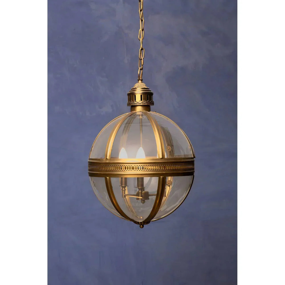 Brass and glass globe pendant light with decorative chain against blue wall background