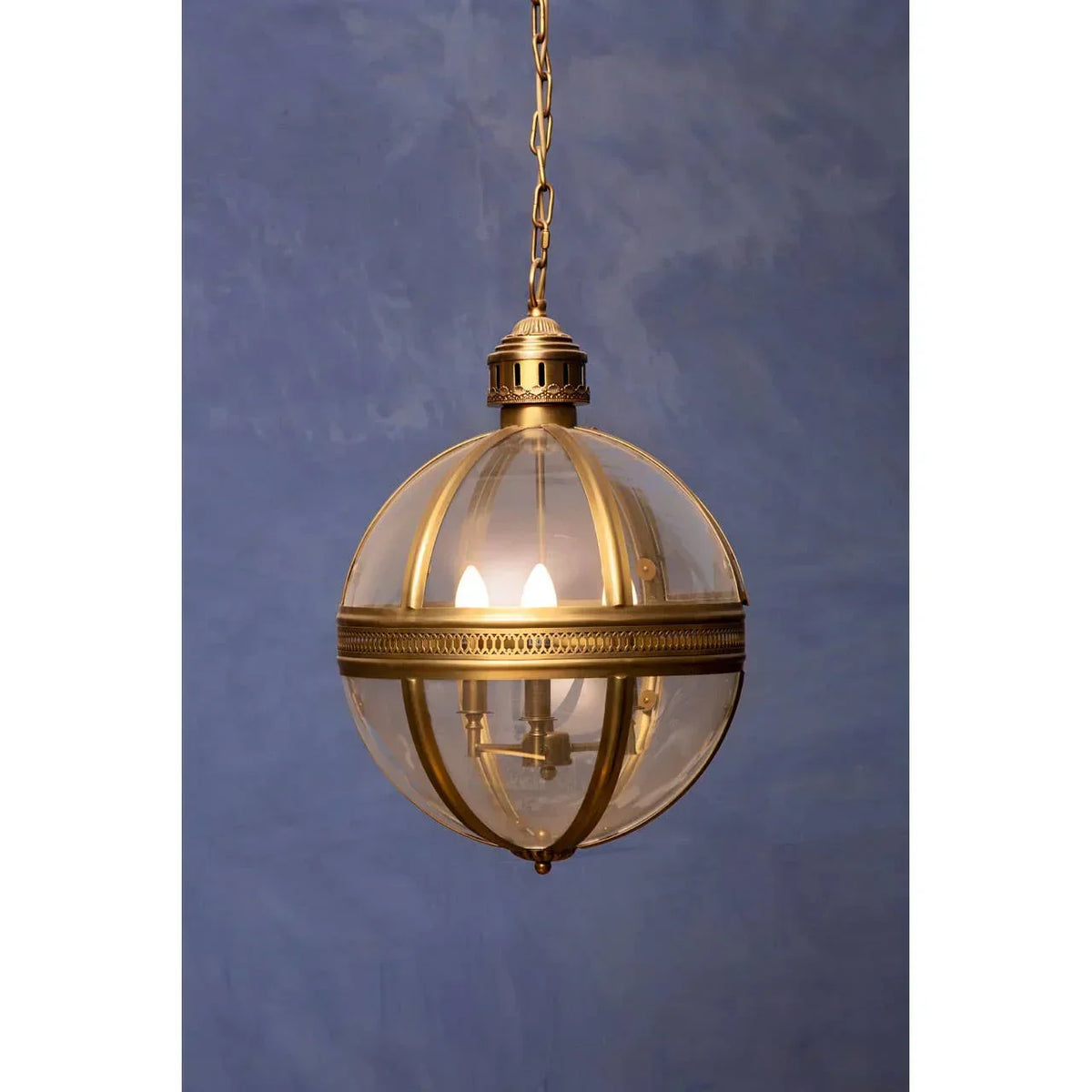 Brass globe pendant light with glass shade and chain against blue wall