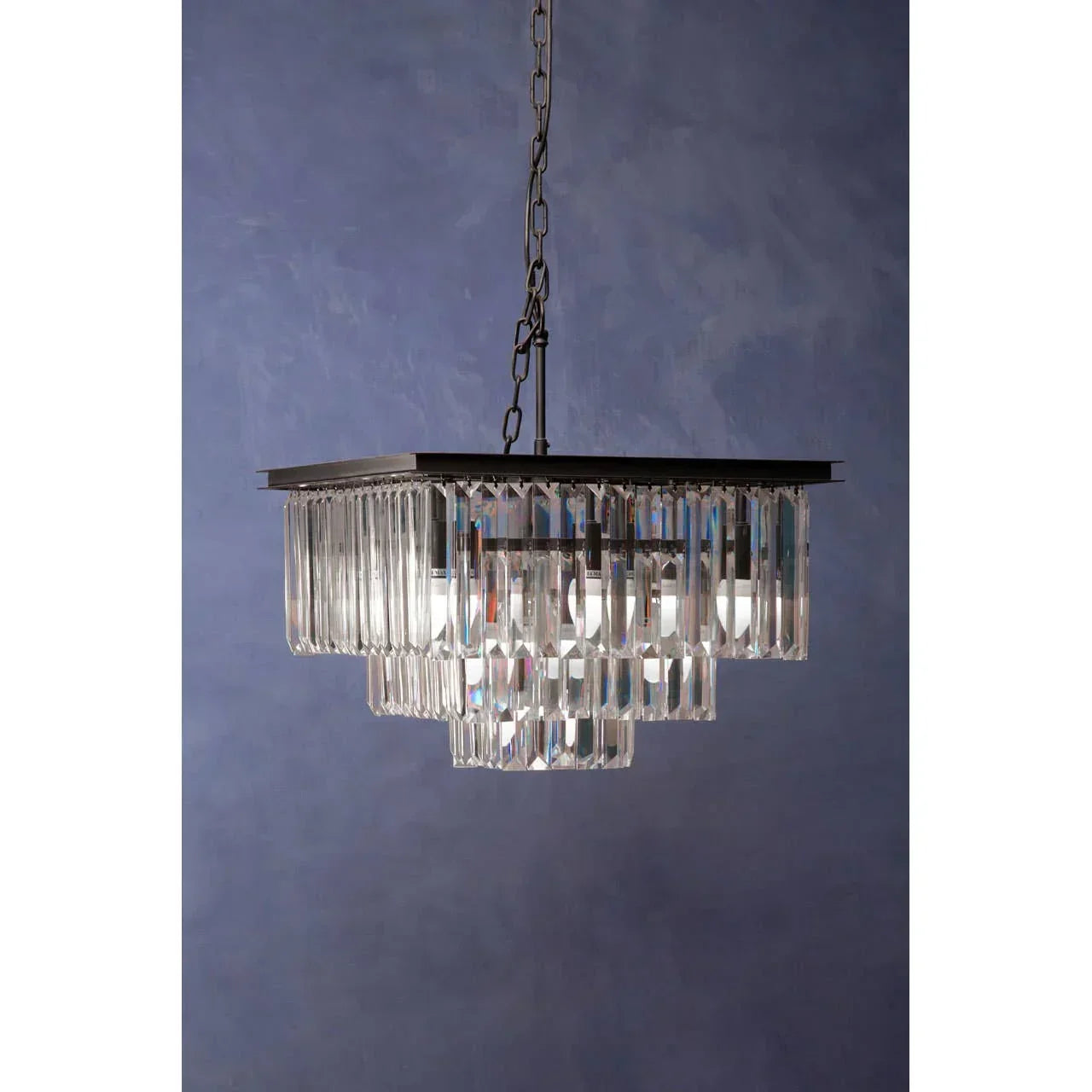 Modern crystal chandelier with rectangular tiers and black chain against blue wall background
