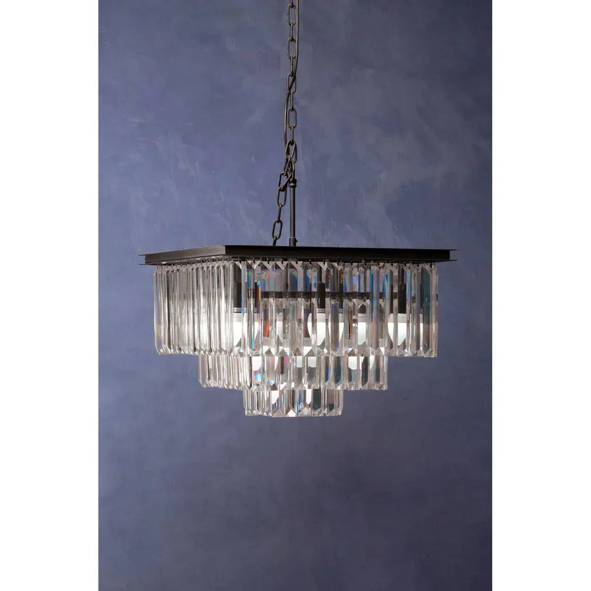 Modern crystal chandelier with rectangular tiers and black chain against blue wall background