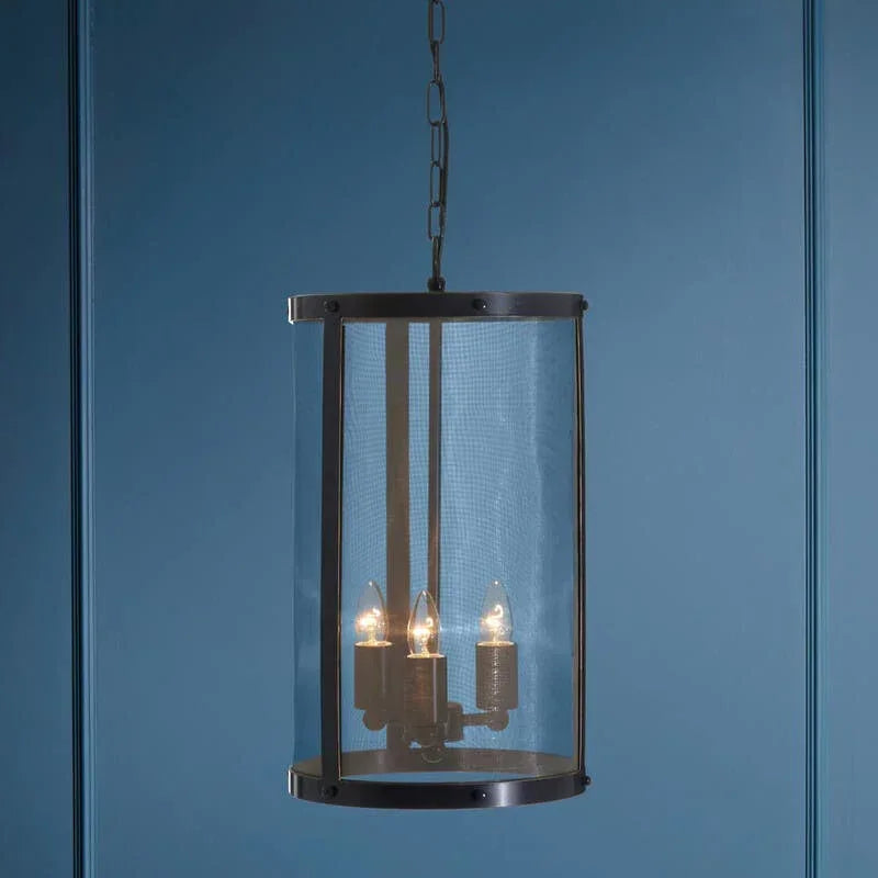 Black metal pendant light with mesh shade and three bulbs against blue wall