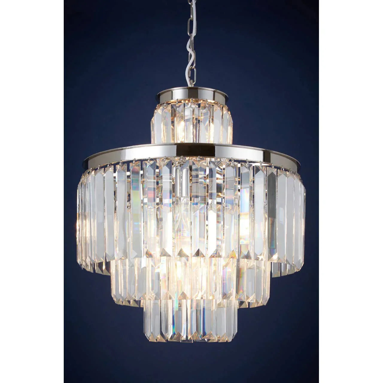 Tiered crystal chandelier with chrome frame suspended on chain against dark blue background