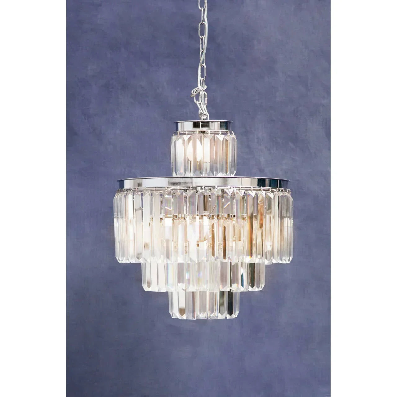 Tiered glass crystal chandelier with chrome frame on chain against blue wall