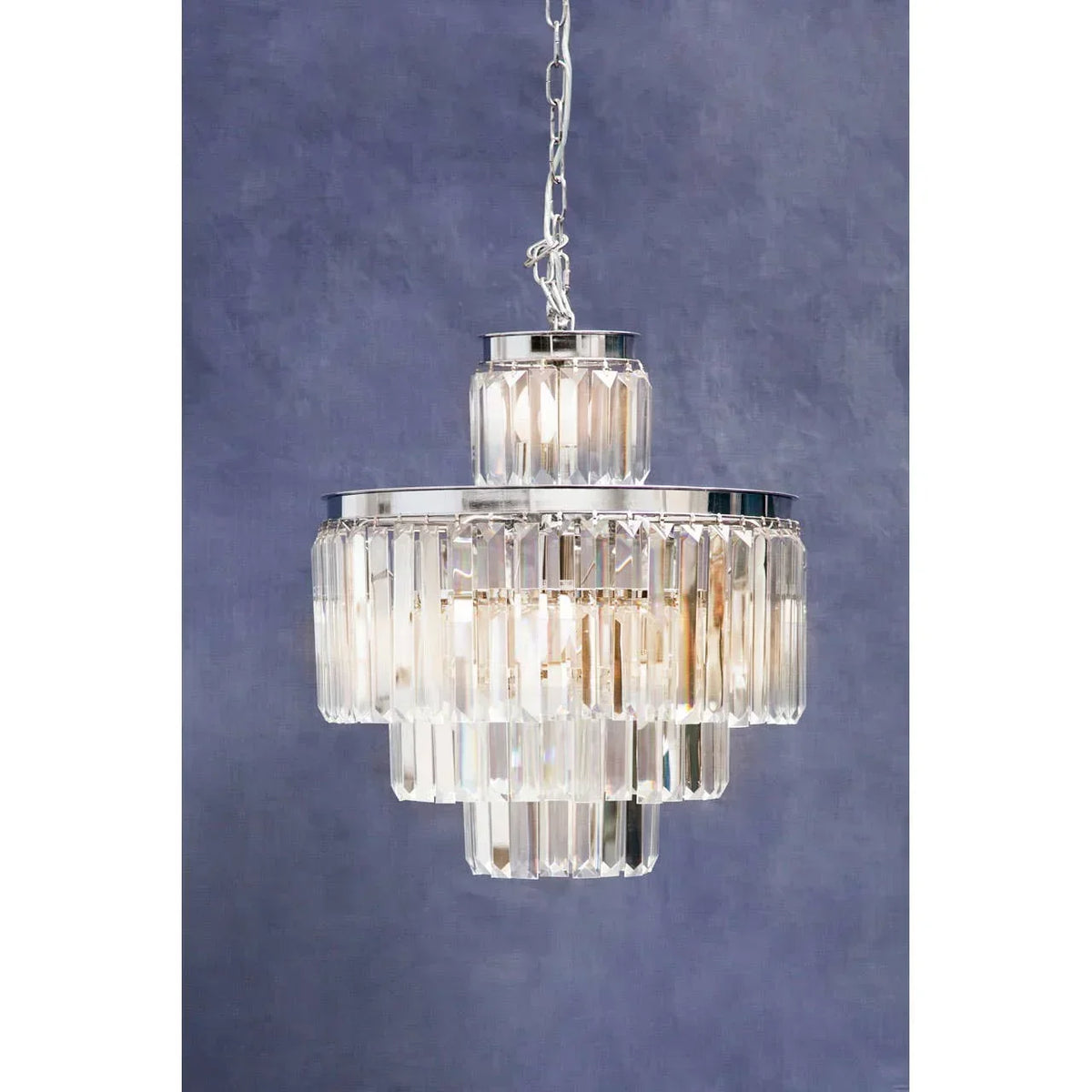 Tiered glass crystal chandelier with chrome frame on chain against blue wall