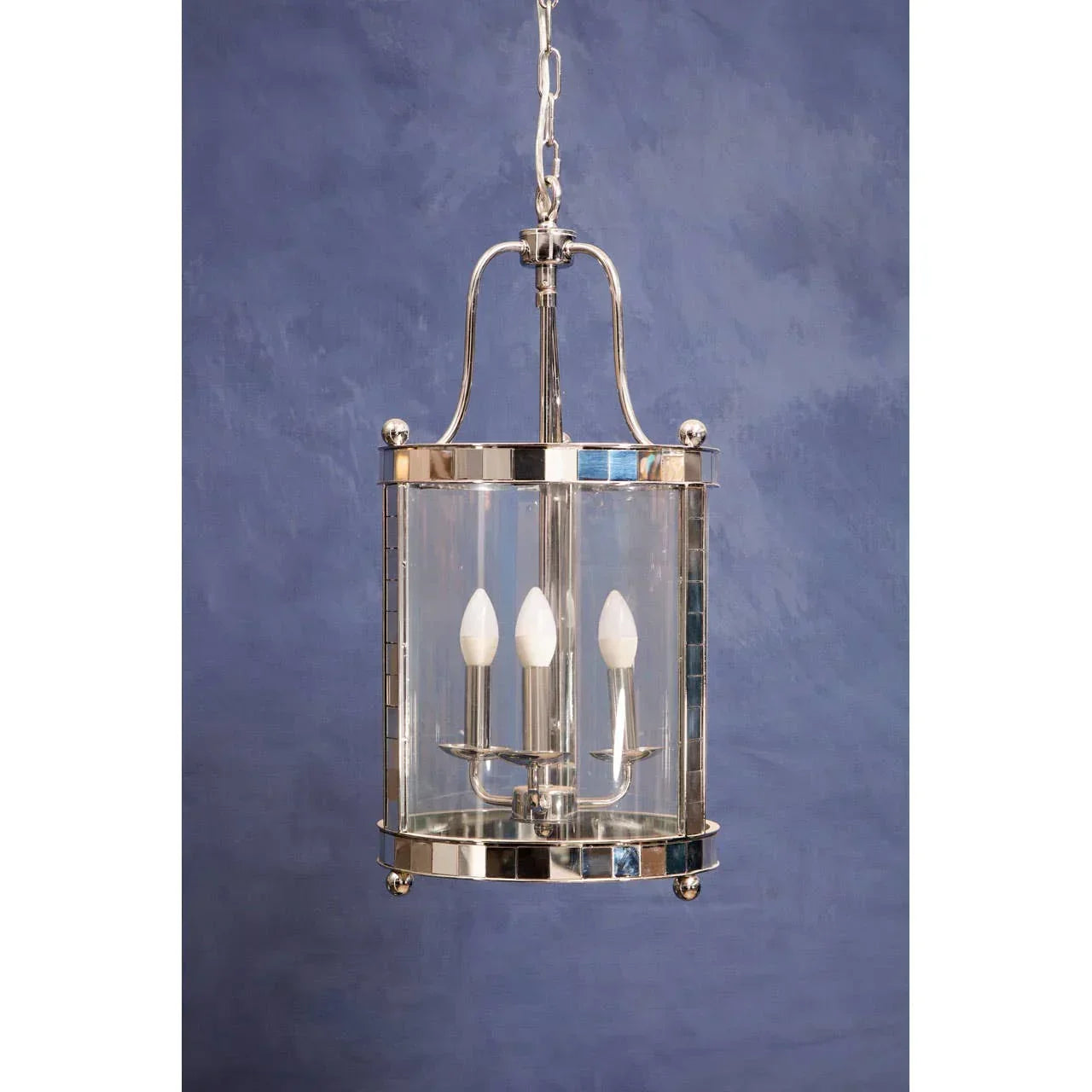 Polished chrome pendant light with three candle bulbs and clear glass shade against blue wall