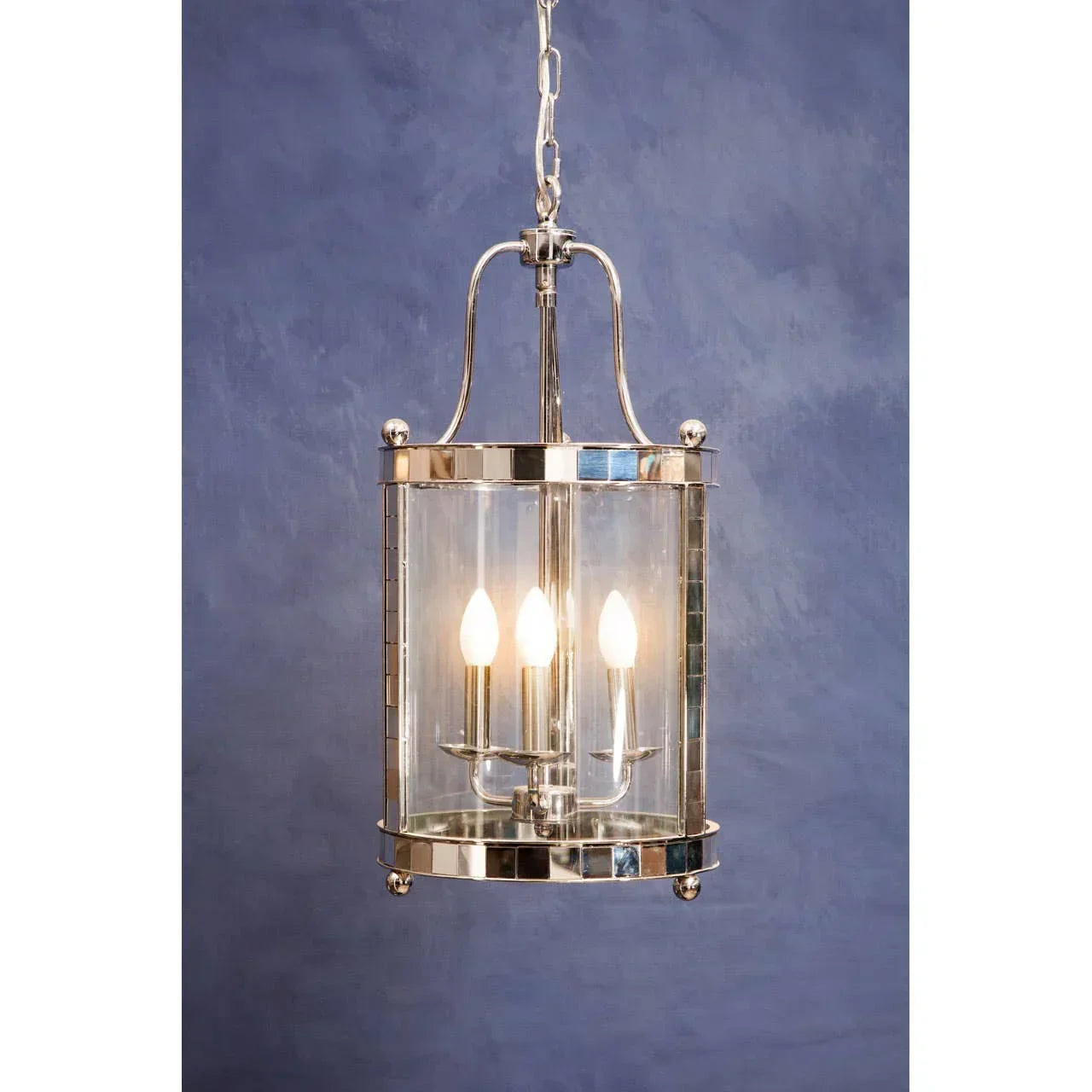 Polished chrome pendant light with three candle bulbs and glass shade against blue wall