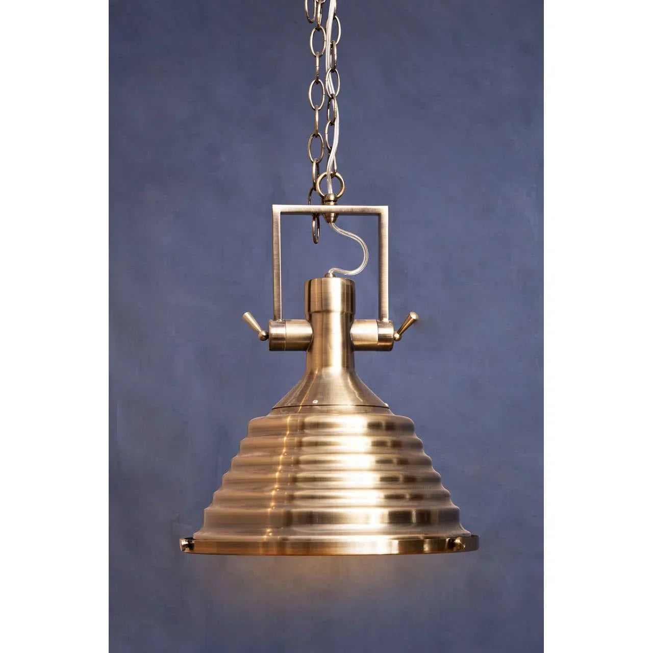 Brass pendant light with ribbed shade and chain hanging against blue background
