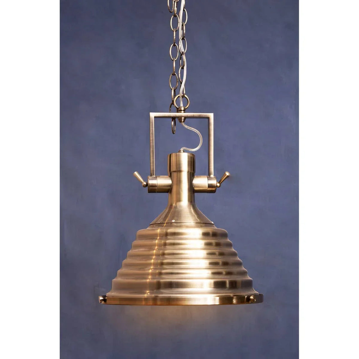 Brass pendant light with ribbed shade and chain hanging against blue background
